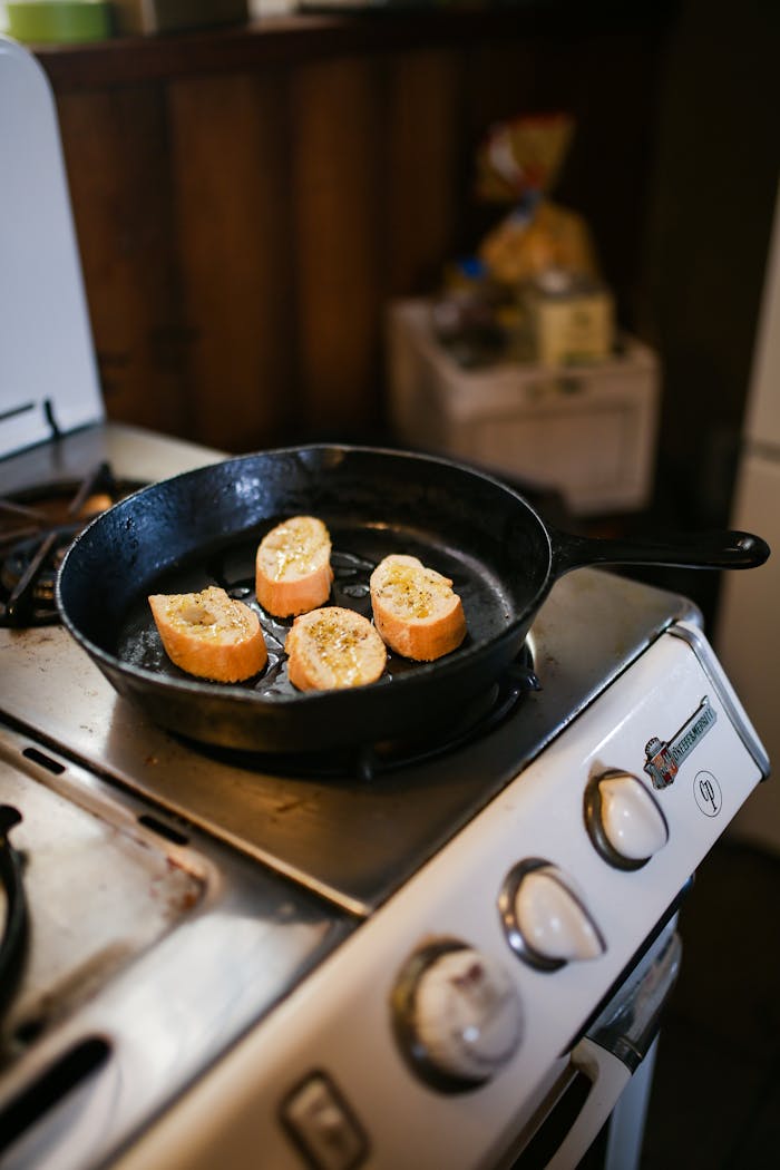 Slices of baguette with herbs cooking in a cast iron skillet on a stove.